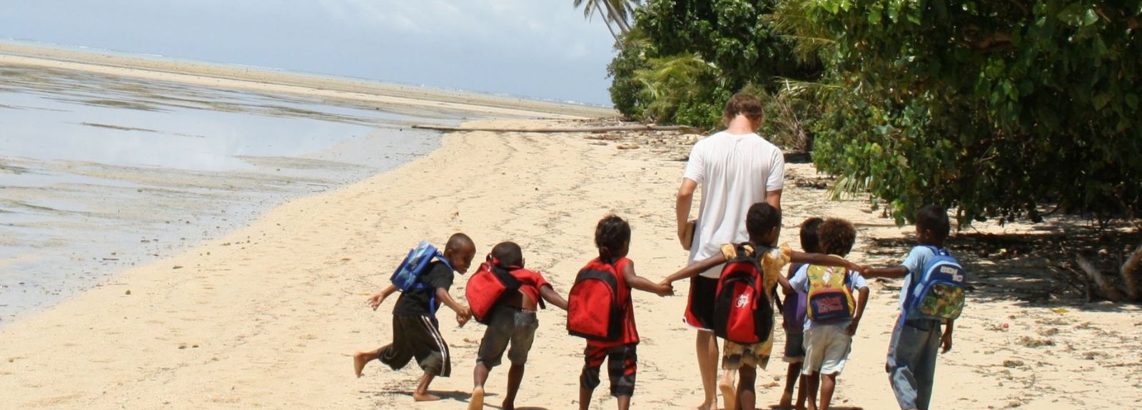 young male student volunteer on a beach leading a group of children